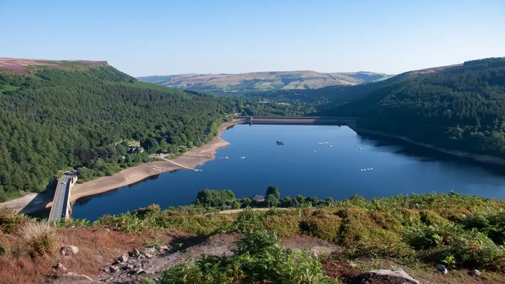 Ladybower Reservoir from Ladybower Tor Side. Bamford Edge rises to the left. To the right, the trees of Win Hill plantation. The dam close to Yorkshire Bridge crosses the reservoir at the far end.