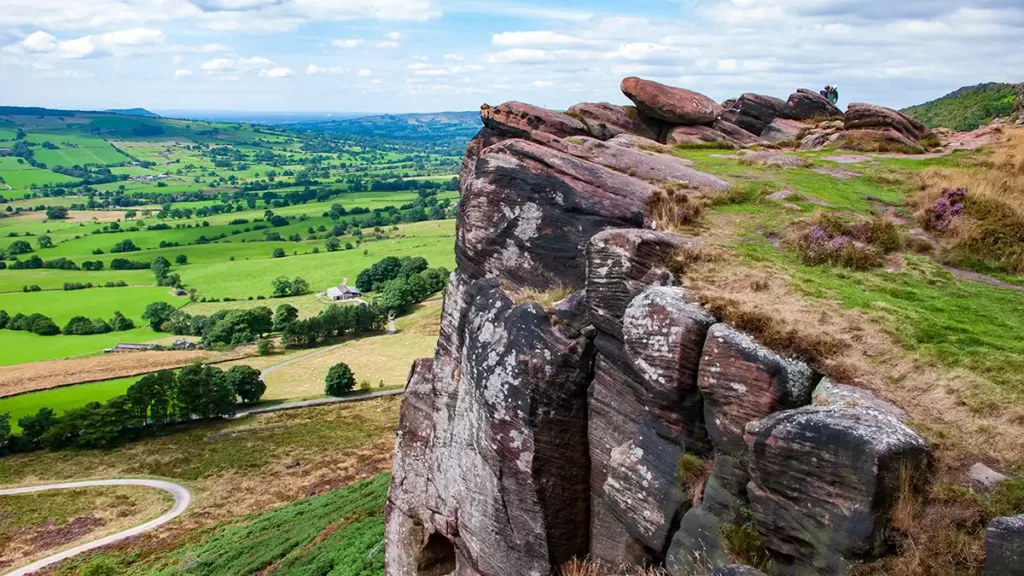 "The gritstone edge of Hen Cloud stands above the fields below. A path runs along the top of the escarpment.