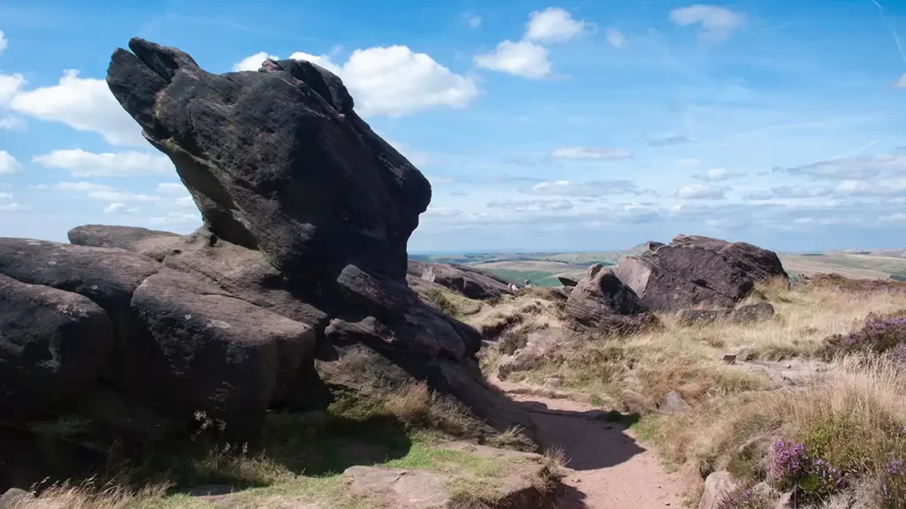 A path runs along the top of The Roaches. Weathered and shaped gritstone rocks of the edge are to the left of the path.